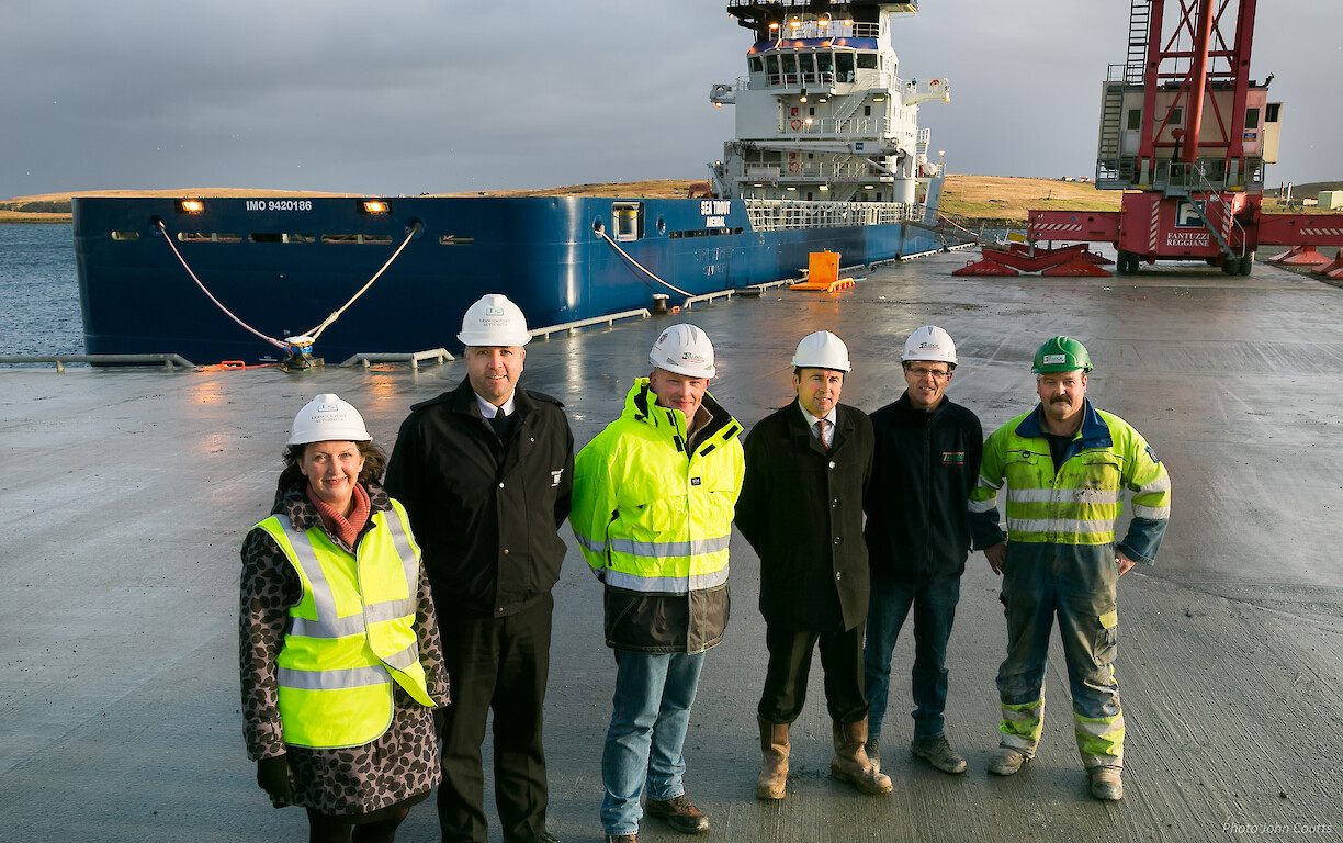Sandra Laurenson, Chief Executive, Lerwick Port Authority; Captain Calum Grains, Harbourmaster, Lerwick Port Authority; George Smith, Director, Tulloch Developments Limited; Andy Sandison, Partner Arch Henderson LLP; Alistair Tulloch and Frank Tulloch, Directors, Tulloch Developments Limited, at the new quay, with the first vessel, Sea Trout, to use it in the background.